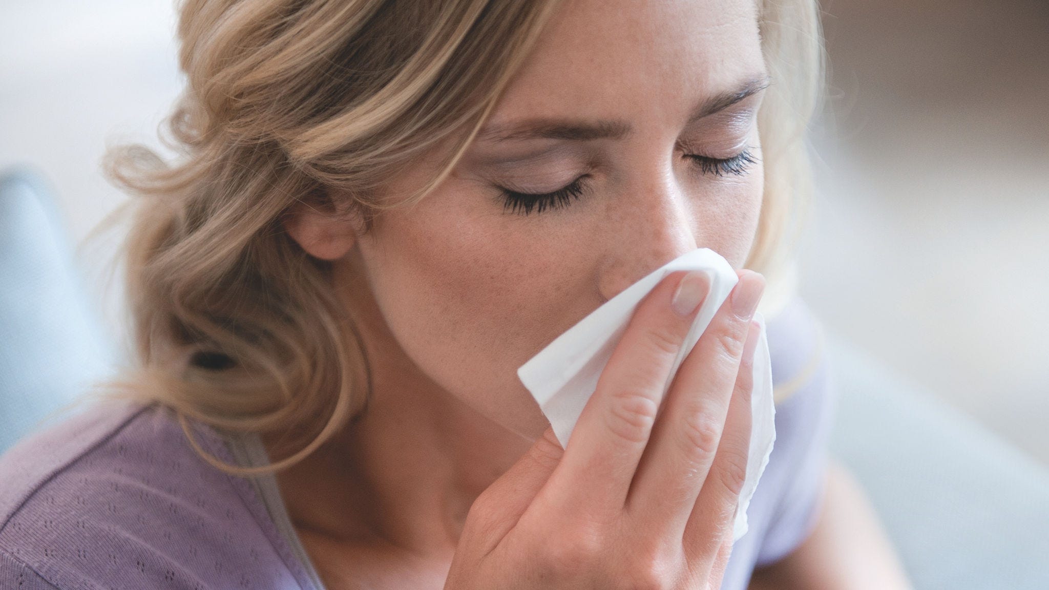 Eine Frau putzt sich wegen Ihrer Pollenallergie die Nase.