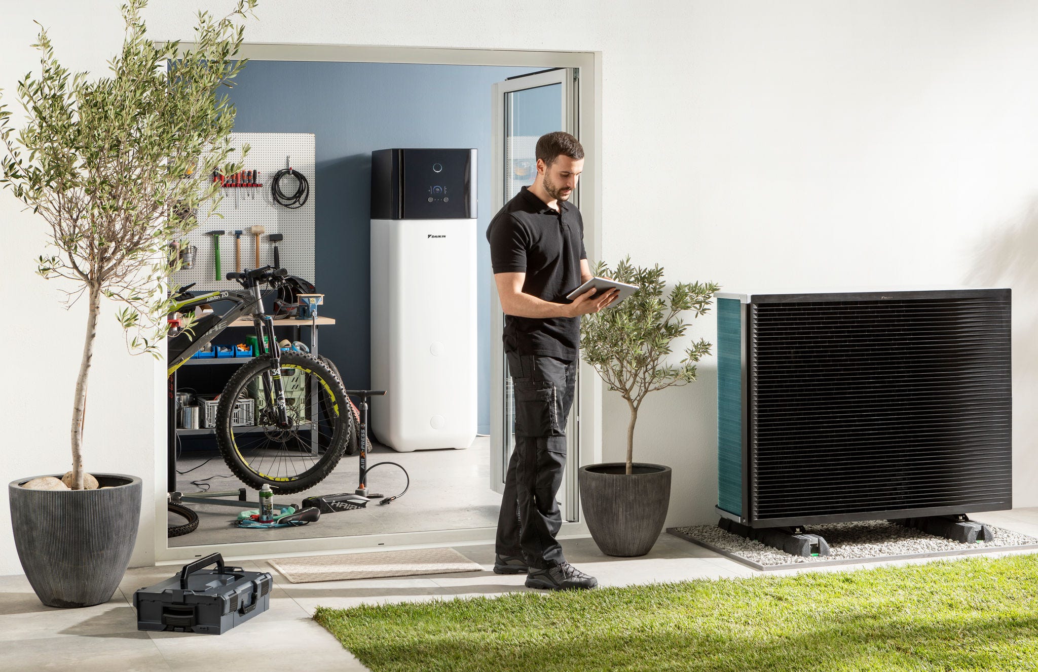 Ein Installateur überprüft ein Außengerät und einen Warmwasserspeicher einer luftgespeisten Wärmepumpe