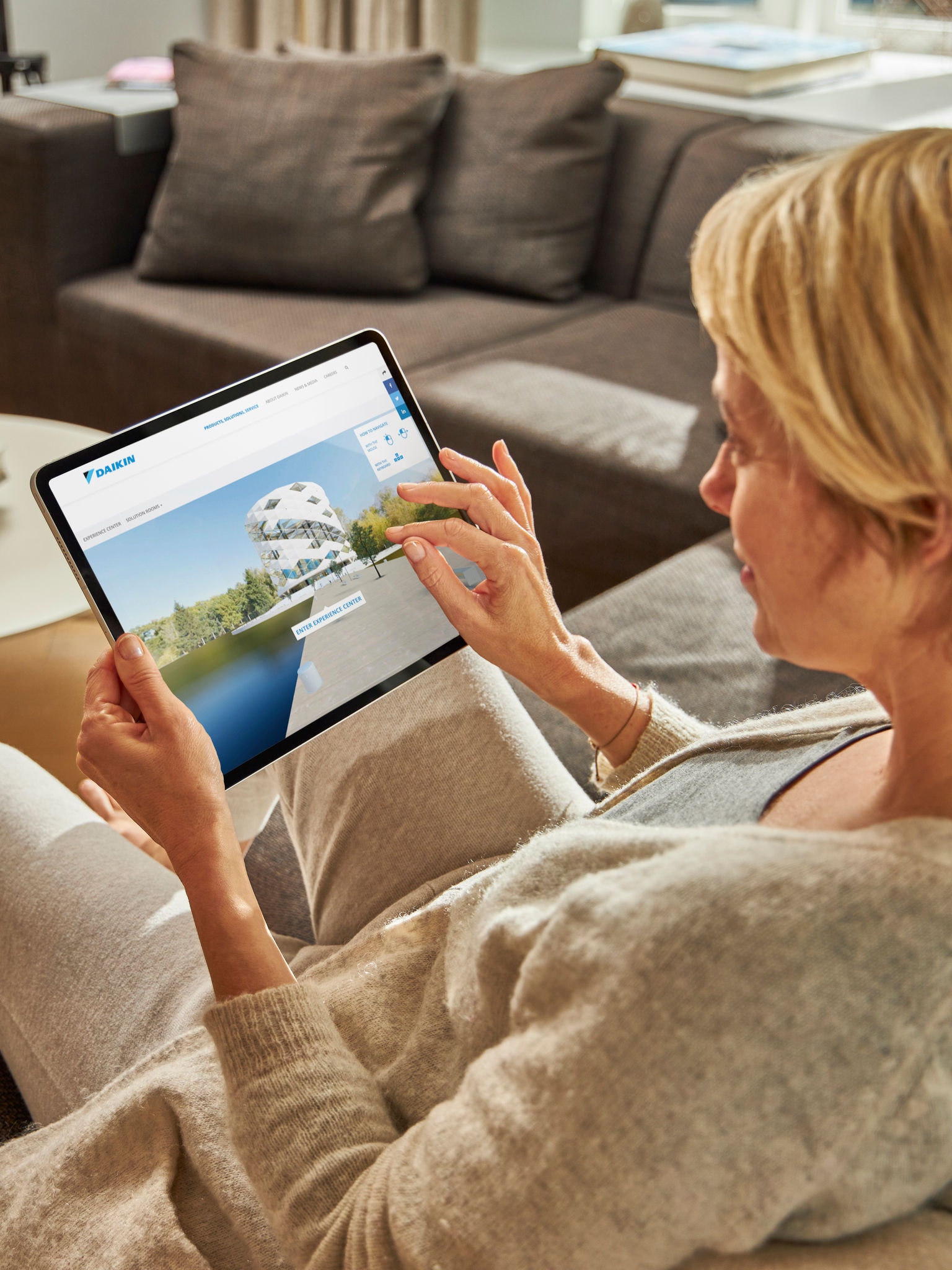 Eine Frau sitzt auf einem Sofa und betrachtet die Klimaanlagen im virtuellen Experience Center auf ihrem Tablet