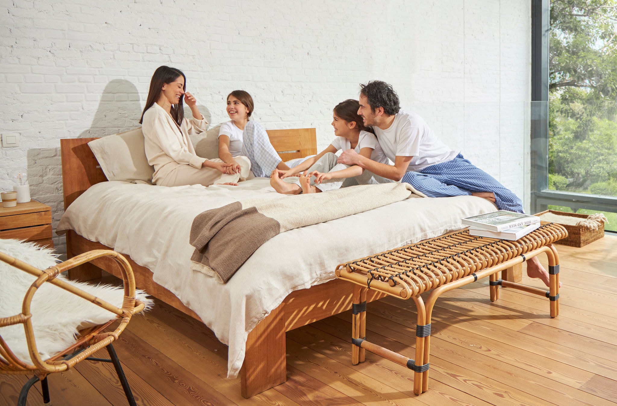 Eine Frau und ein Mann sitzen auf einem Bett mit zwei jungen Mädchen, entspannt, lachend und mit gesunder Luft.