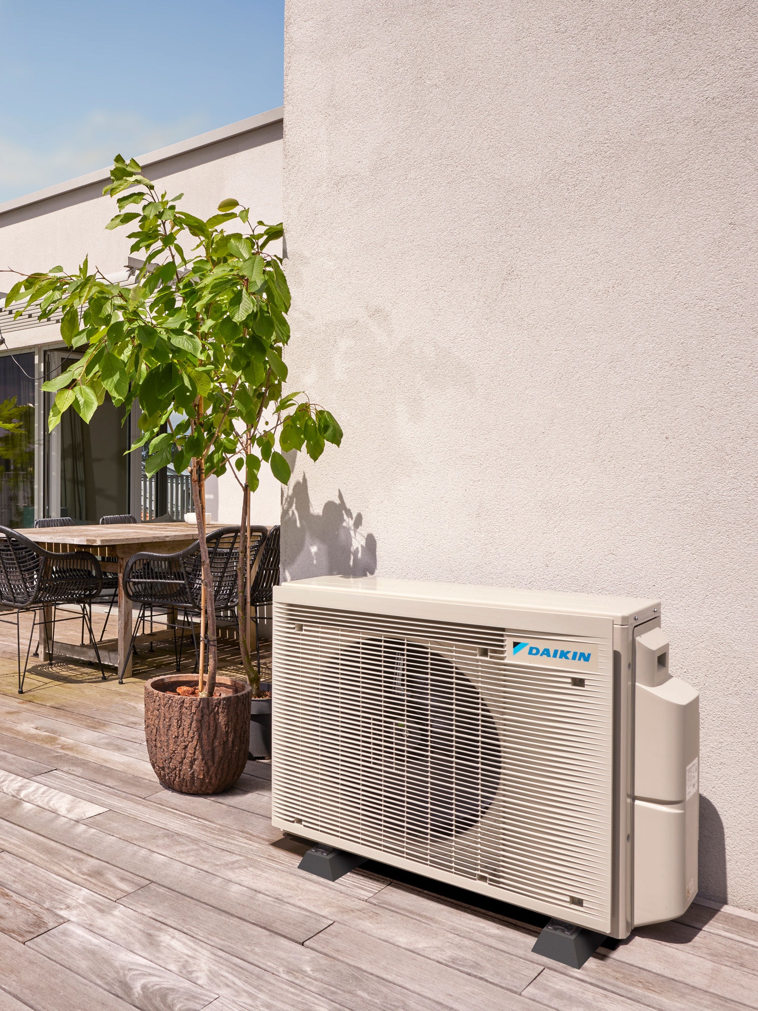 Außenwärmepumpe, unauffällig an einer Wand positioniert und im Schatten von Bäumen