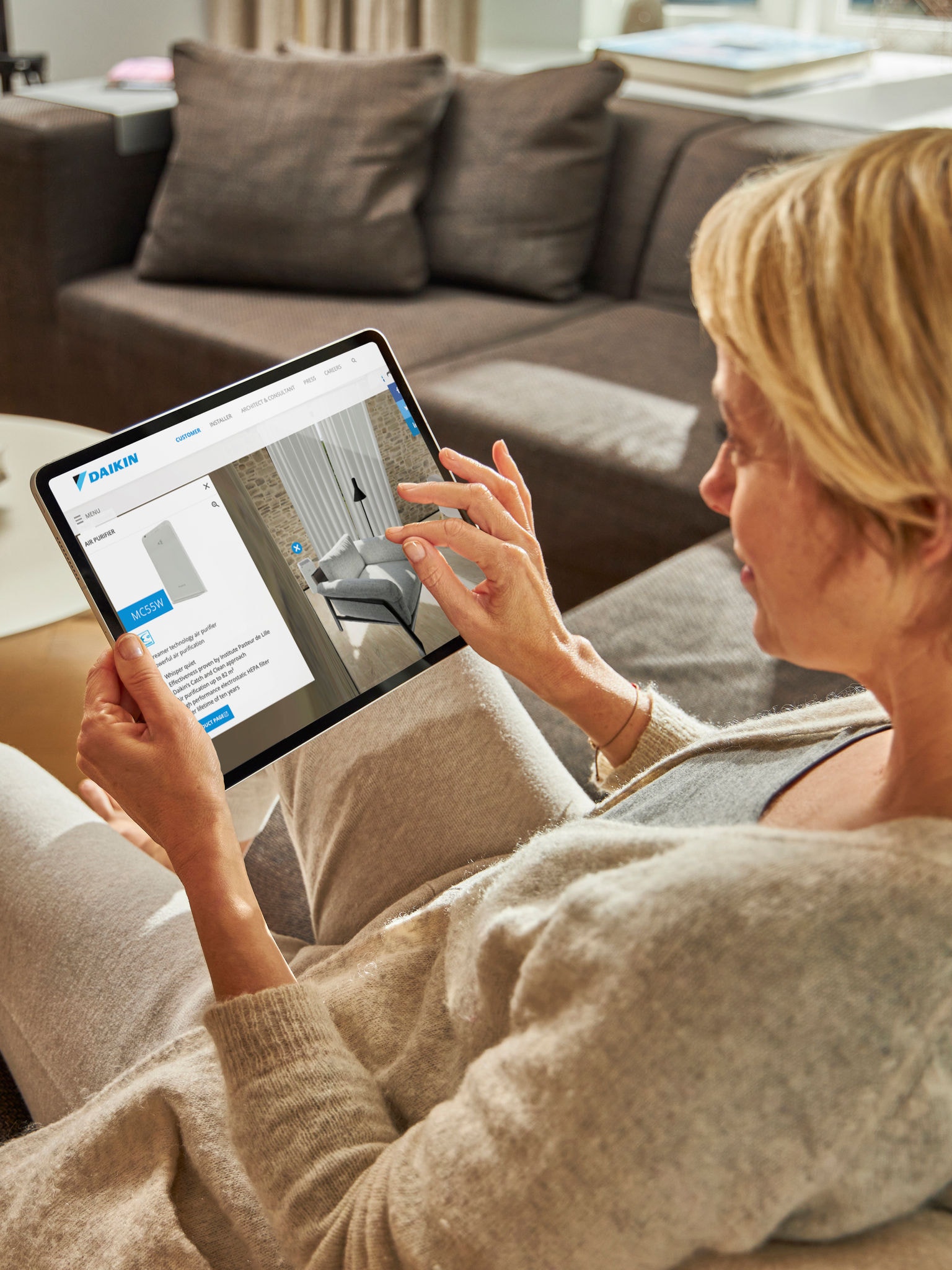 Eine Frau sitzt auf einem Sofa und betrachtet die Klimaanlagen im virtuellen Experience Center auf ihrem Tablet