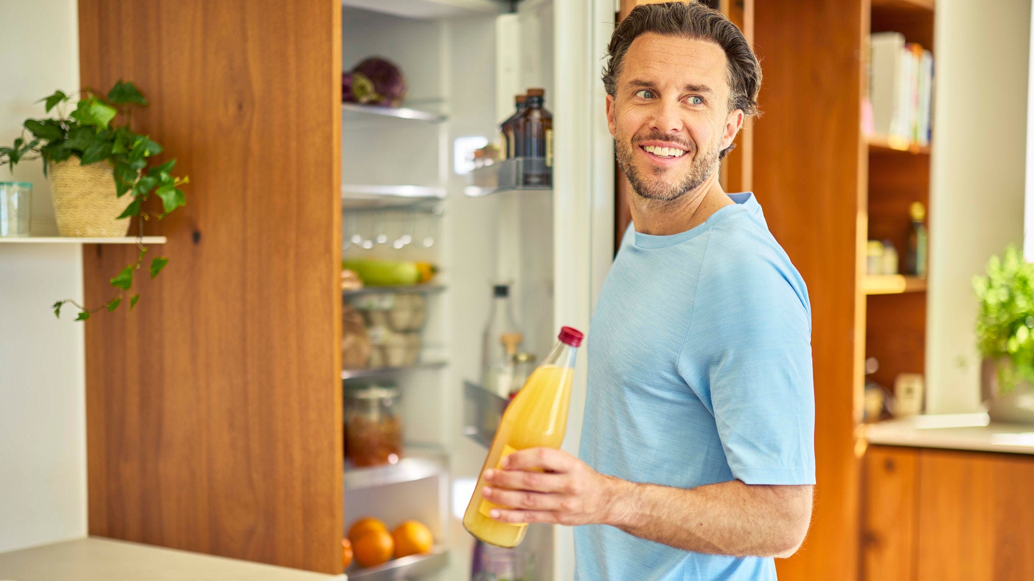 Ein Mann in einer modernen Küche entnimmt einem Kühlschrank eine Flasche Orangensaft