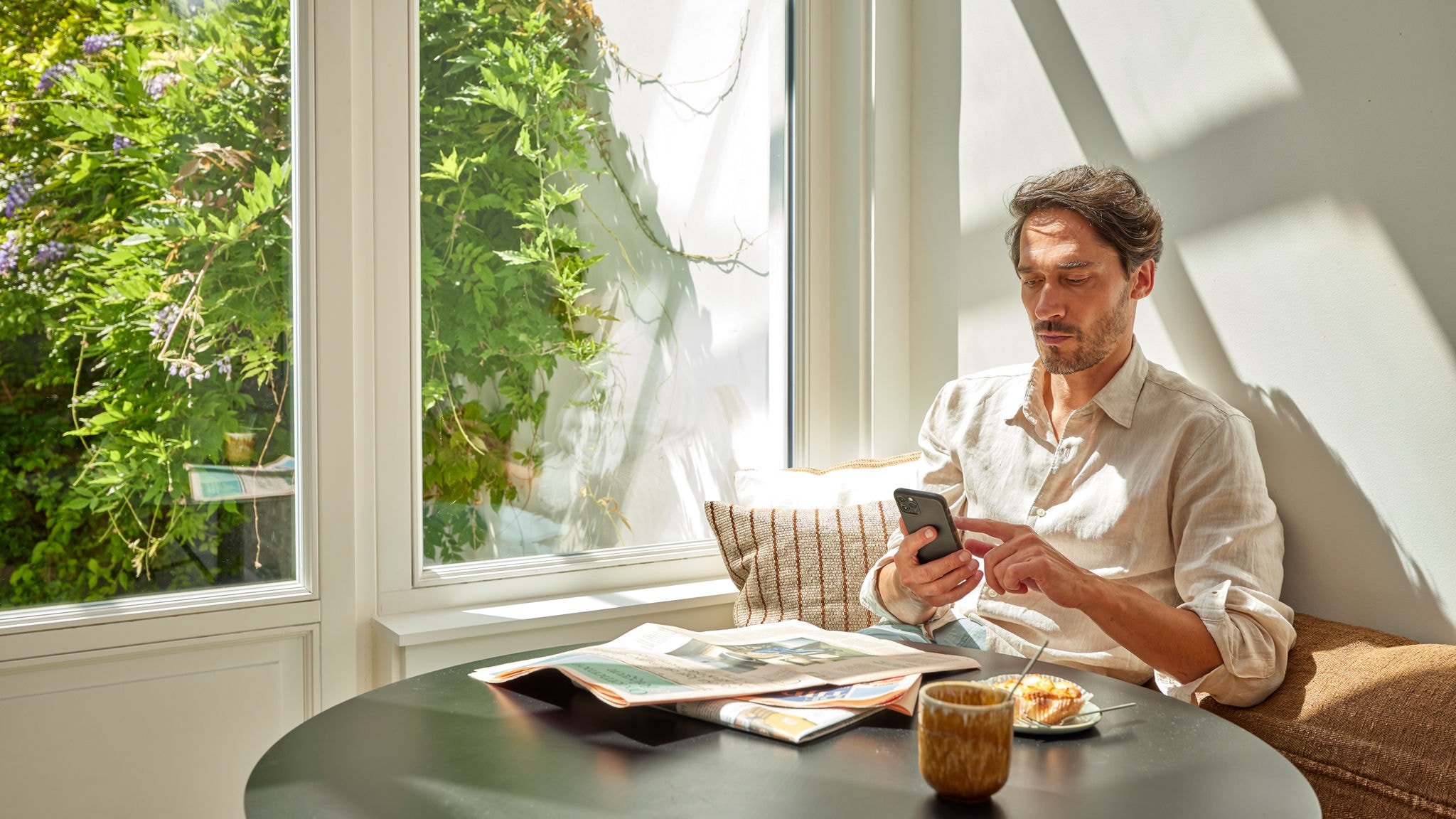 Ein Mann in einem hellen Zuhause überwacht und bedient anhand seines Smartphones eine Luft-Luft-Wärmepumpe für energiesparsamen Komfort.