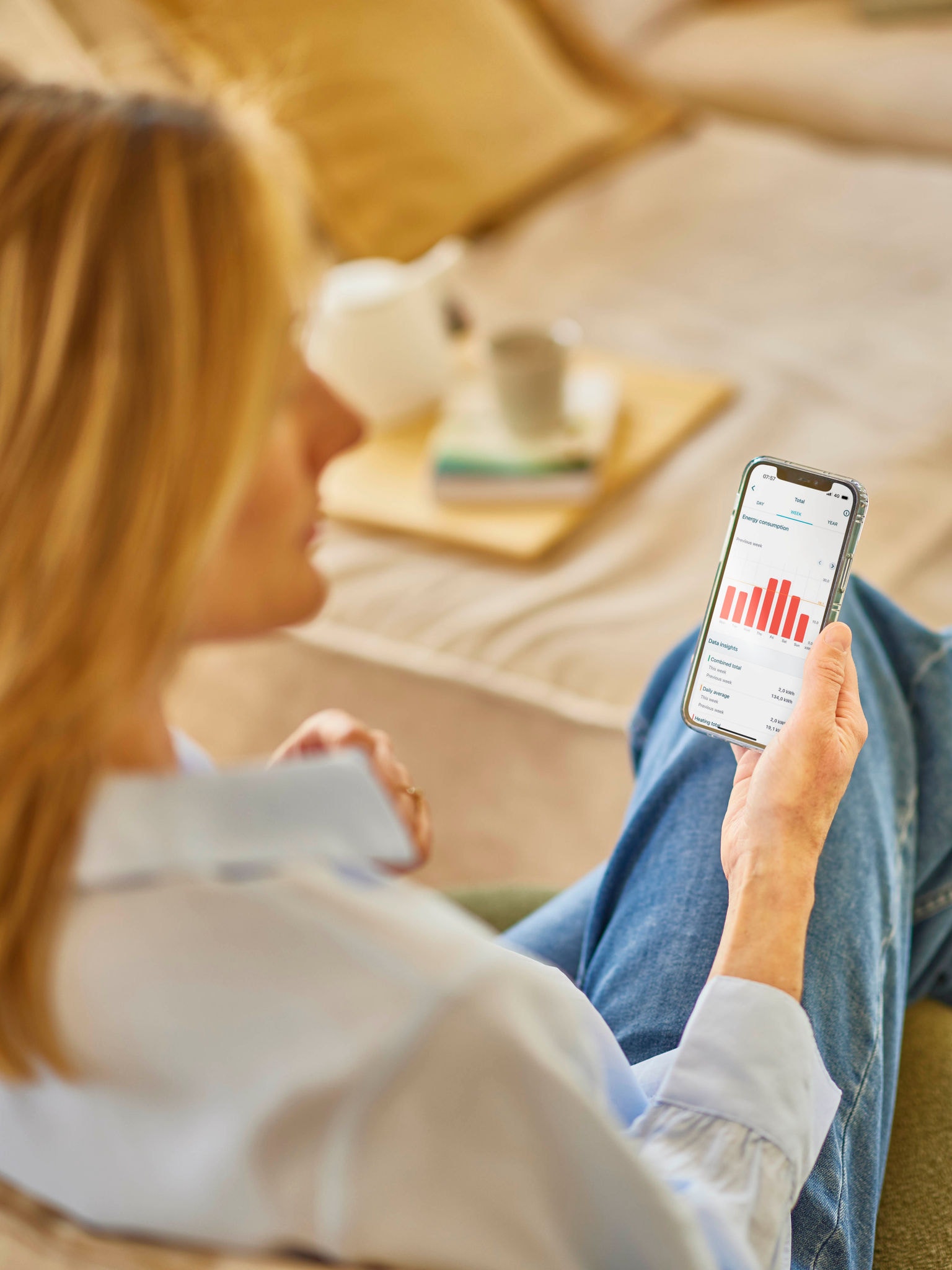 Eine Frau mit blondem Haar kontrolliert anhand einer App auf ihrem Smartphone den Energieverbrauch