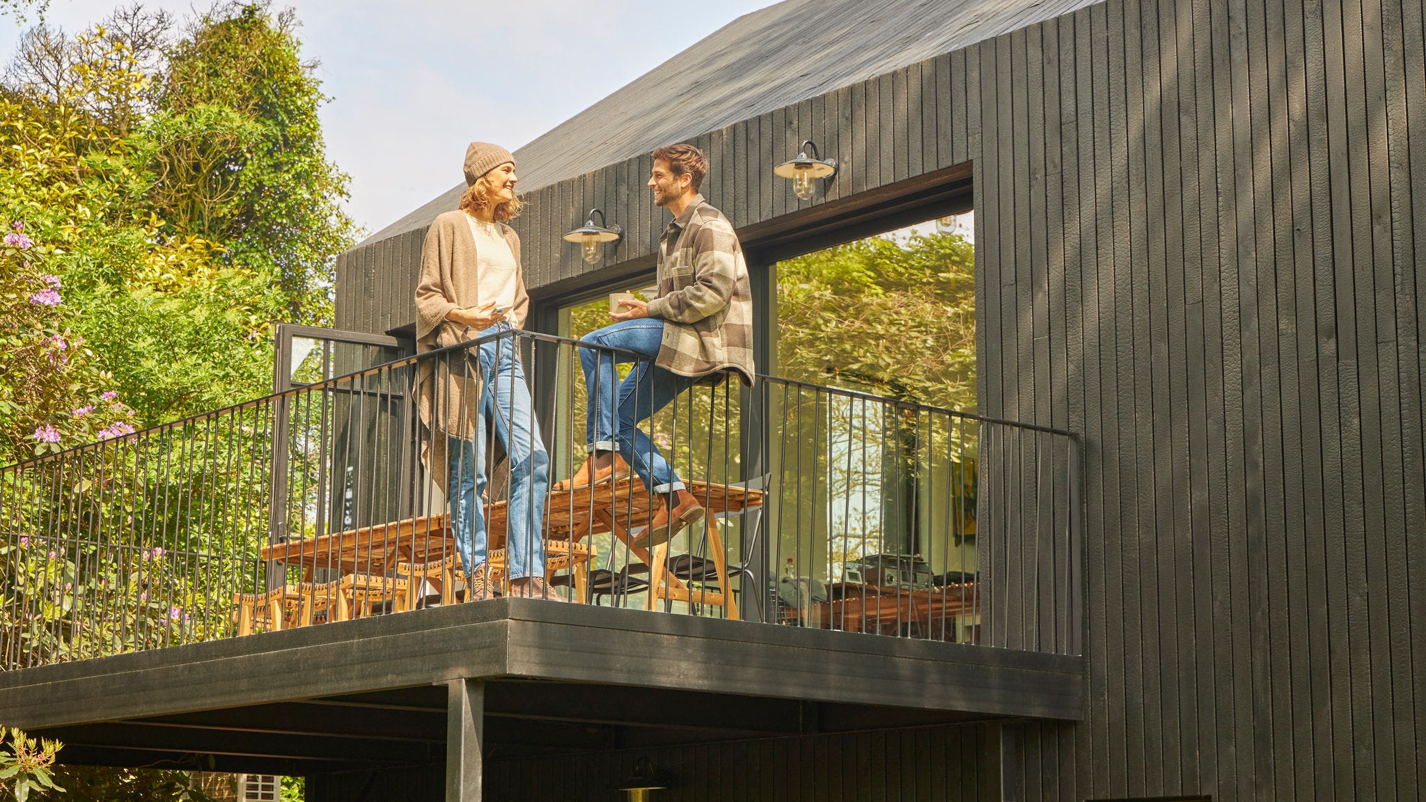Ein Pärchen unterhält sich auf der Terrasse eines von Natur umgebenen modernen Holzbungalows und genießt die frische Luft und das energieeffiziente Leben