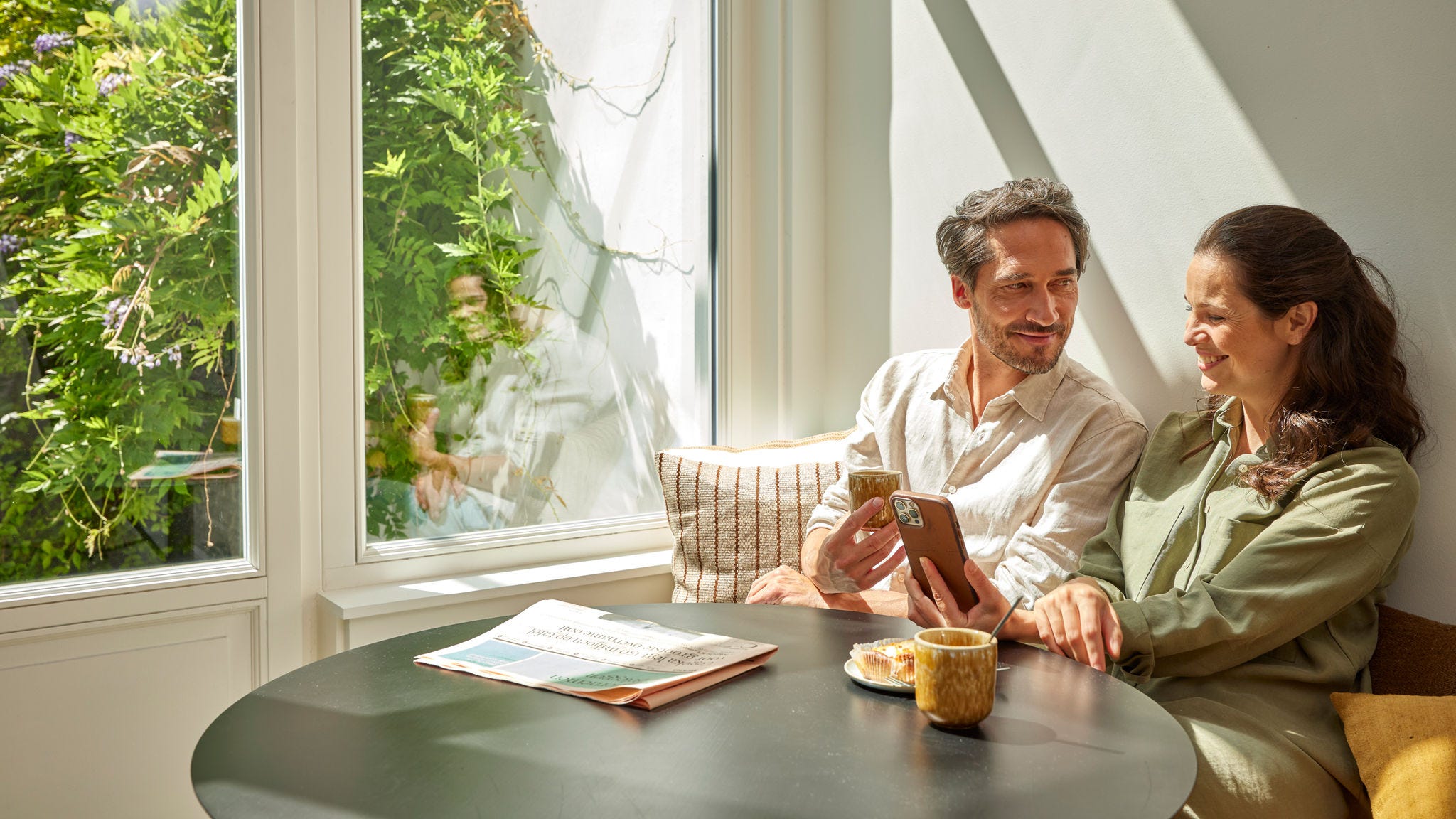 Ein Paar trinkt Kaffee und überprüft die Energieeinsparungen auf ihrem Smartphone, um die Kosteneinsparungen durch den Einsatz einer Wärmepumpe zu veranschaulichen