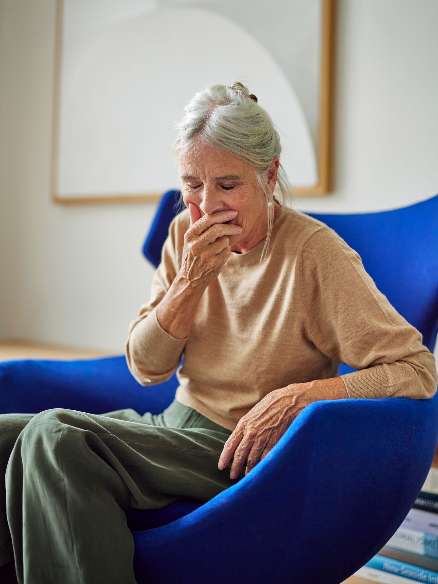 Eine Frau sitzt in einem Sessel und hustet aufgrund ihres Asthmas.