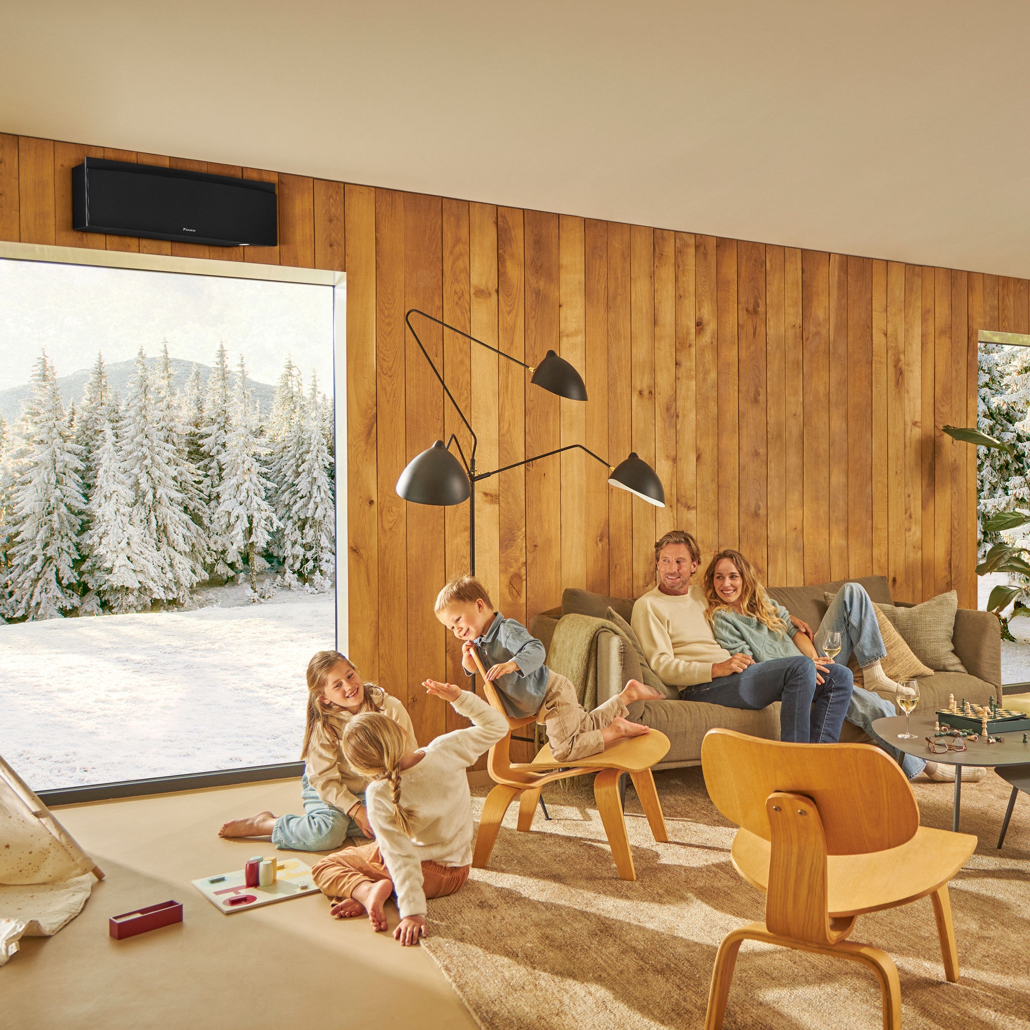 Eine Familie genießt ihr warmes, gemütliches Wohnzimmer mit einer Winterlandschaft im Freien – hier wird die Effektivität unserer Heiz-, Kühl- und Lüftungslösungen bei der Schaffung eines ganzjährig komfortablen Raumklimas unter Beweis stellt.