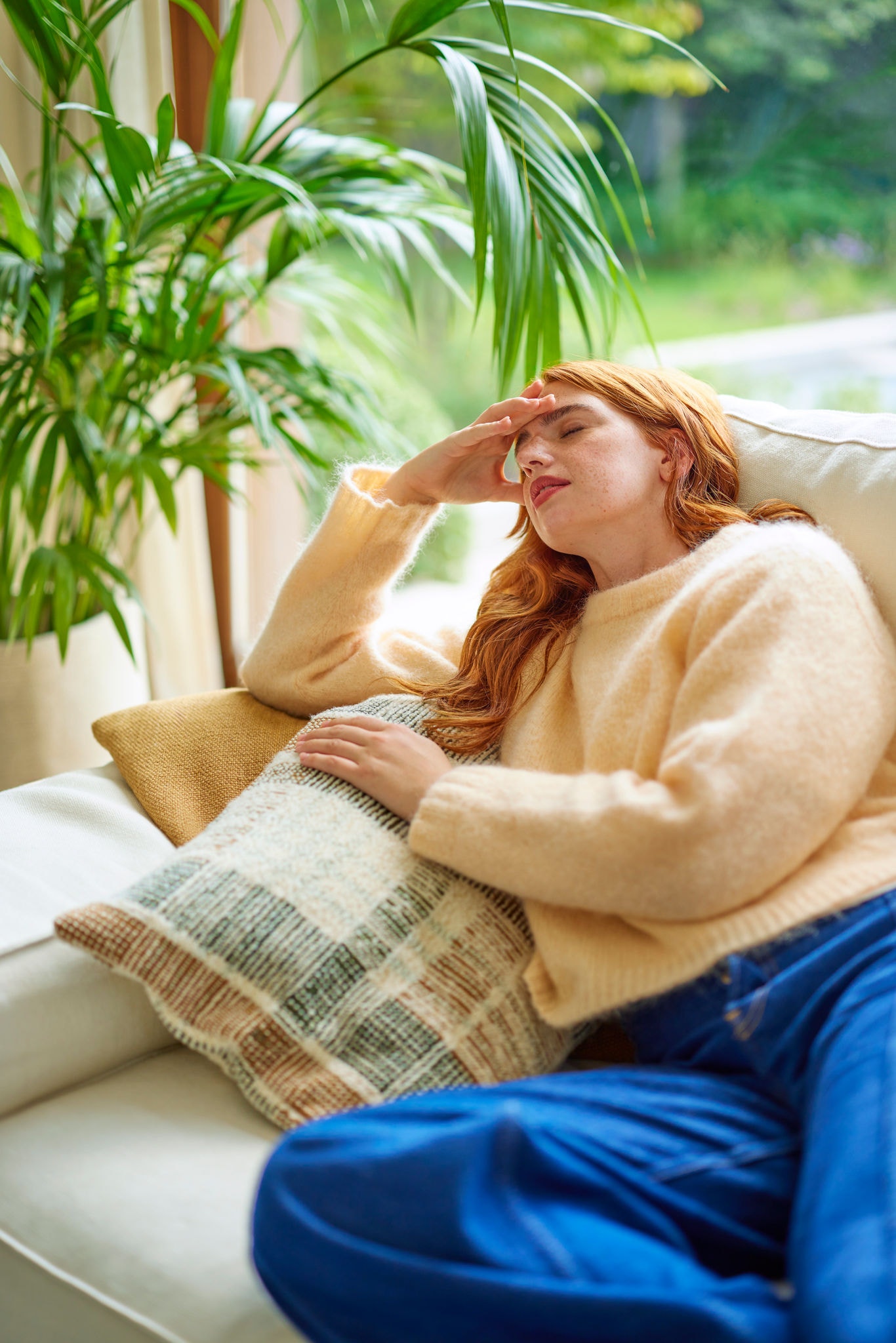 Sich unwohl fühlendes Mädchen mit Kopfschmerzen liegt auf dem Sofa und verdeutlicht so die Auswirkungen schlechter Luftqualität und die Notwendigkeit einer ausreichenden Lüftung