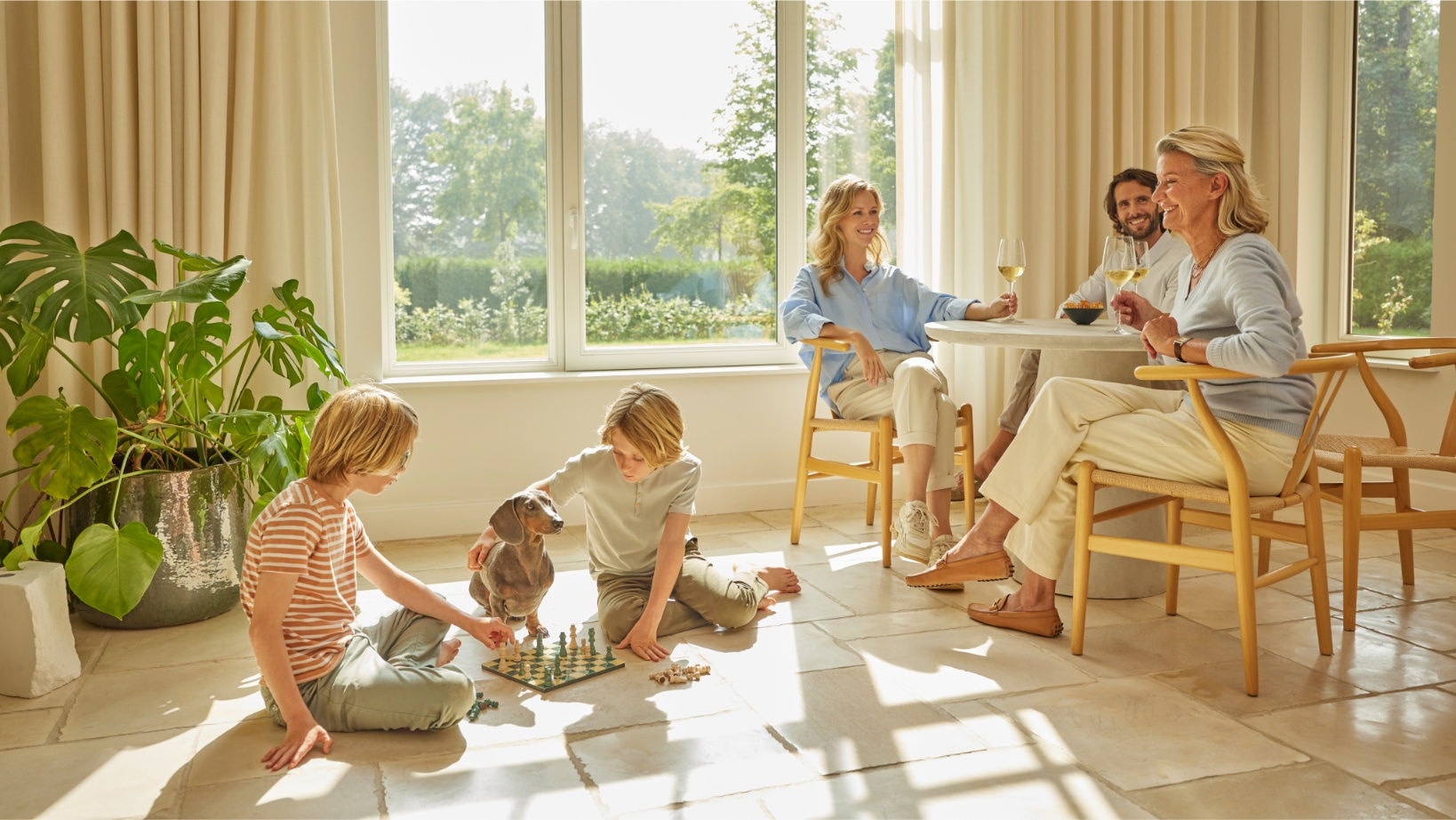 Eine Familie genießt die saubere Raumluft mit dem DAIKIN Luftreiniger, während die Kinder Schach spielen und die Erwachsenen sich mit Getränken in einem hellen, gut belüfteten Wohnzimmer entspannen