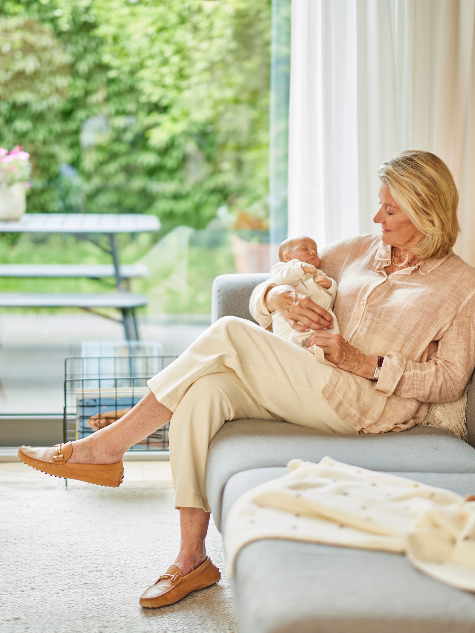 Frau, die ein Baby im Arm hält, während sie auf einem Sofa in einem angenehm beheizten Raum sitzt.