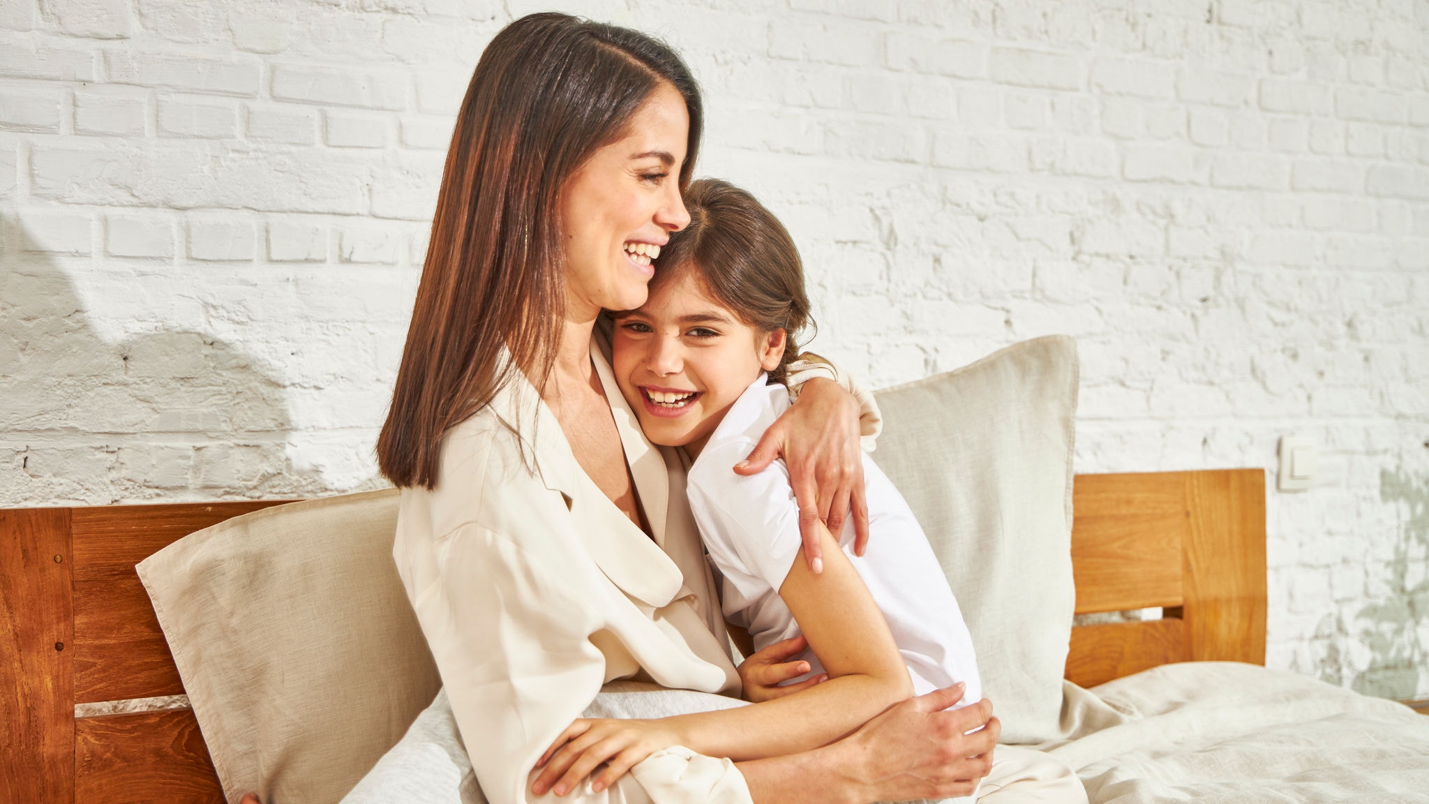 Eine Mutter und die kleine Tochter lächeln und umarmen sich, während sie auf einem Bett sitzen