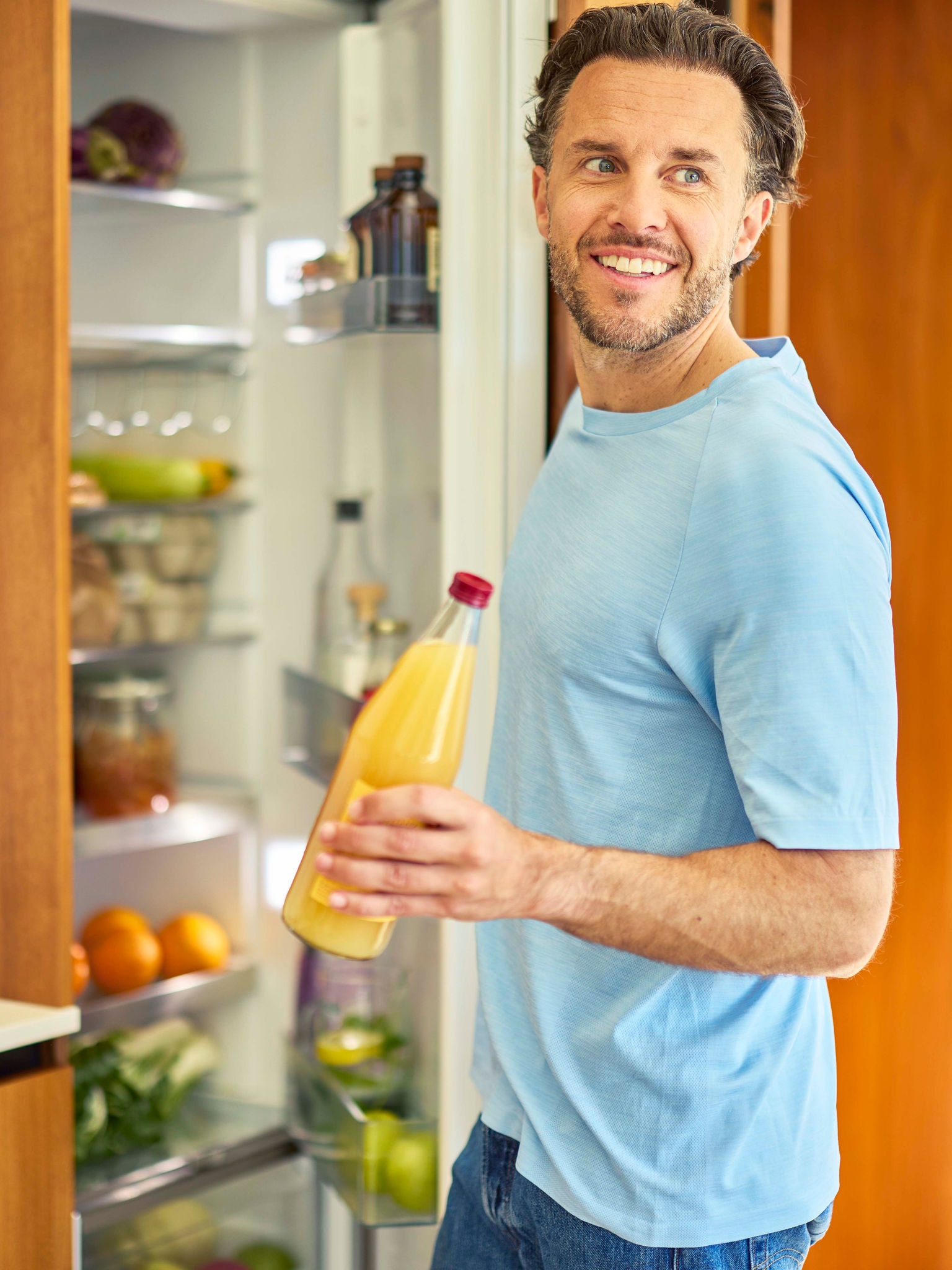 Ein Mann öffnet einen Kühlschrank und entnimmt eine Flasche Orangensaft